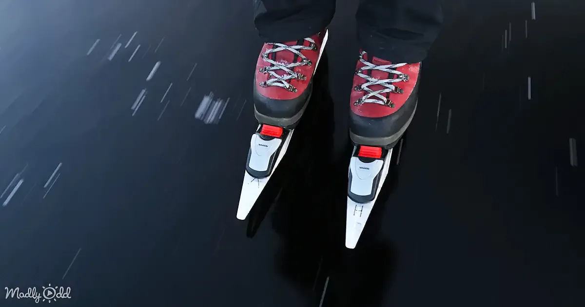 A person wearing red and black roller skates glides on a dark, reflective surface.