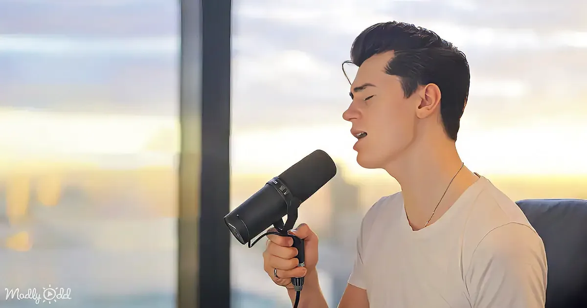 A person in a white shirt sings into a microphone, with a blurred cityscape and sky in the background.