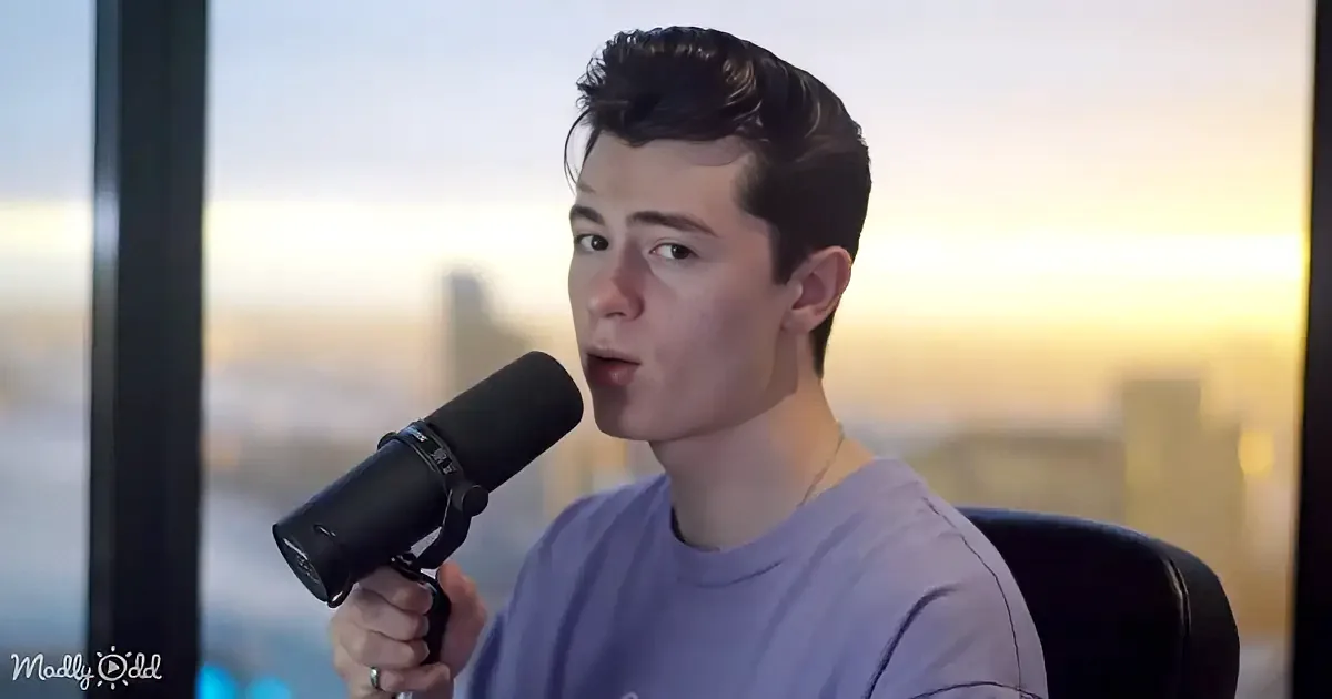 A person in a purple shirt speaks into a microphone, with a cityscape and sunset in the background.
