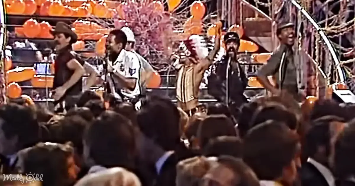 A band performs on stage with vibrant orange balloons and a lively crowd in the foreground.