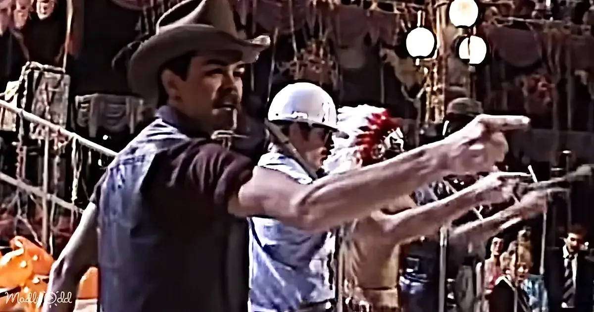 A man in a cowboy hat points a gun, with another person in a white helmet aiming a crossbow in the background.