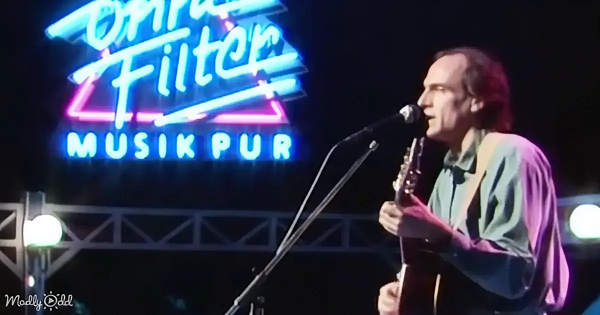 A man plays guitar and sings on stage with a neon sign reading "Filter Musik Pur" in the background.
