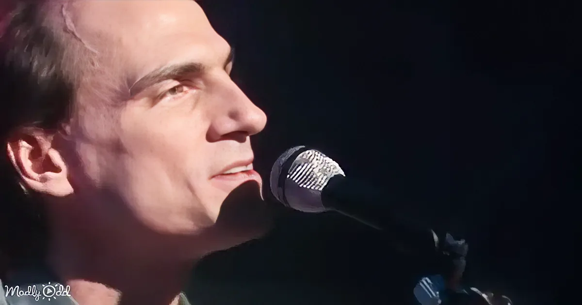 A man in a green shirt sings into a microphone on stage with a blue background.