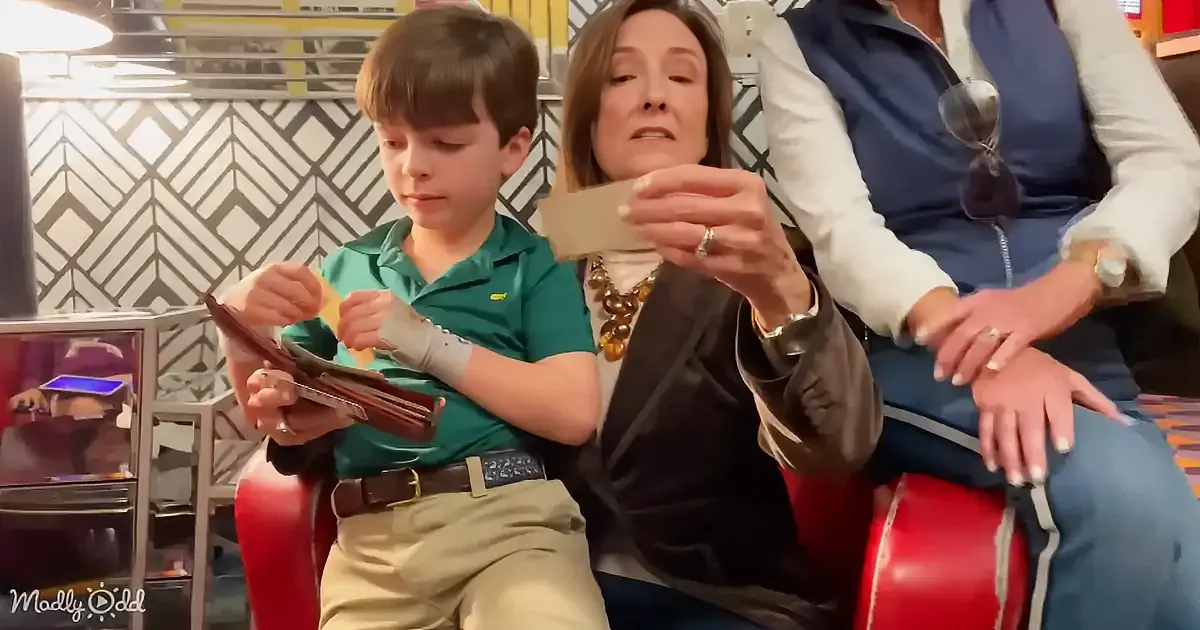 A boy in a green shirt sits on a red chair, holding a tablet, while a woman next to him looks at a phone.