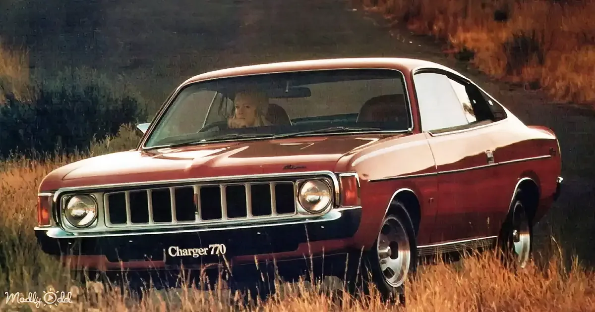 A vintage red Charger 770 car is parked in a grassy field with a person inside.