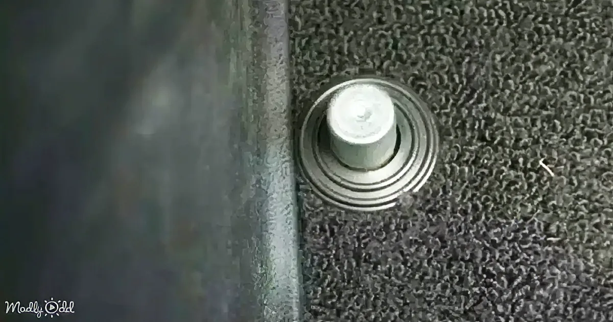 A metallic button with concentric rings sits on a textured gray surface, bordered by a darker material.