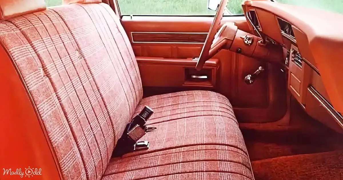A vintage car interior with plaid fabric seats, wood paneling, and a steering wheel.
