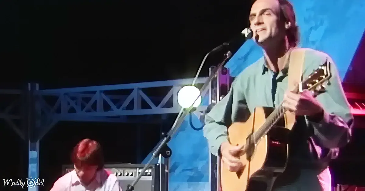 A man sings into a microphone, wearing a green shirt, with a blurred background of red and purple hues.