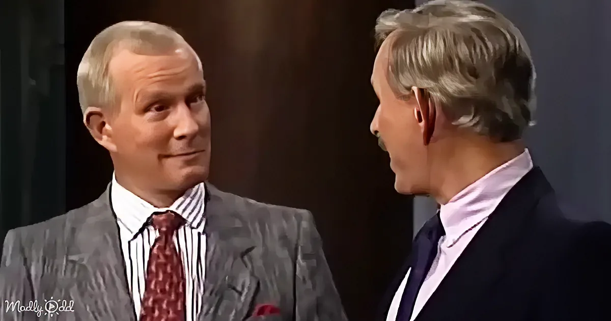 Two men in suits, one in a gray suit with a red tie, the other in a dark suit with a pink shirt, appear to be engaged in...