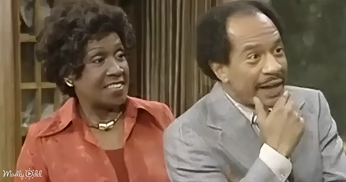A woman in a red blouse and necklace smiles, while a man in a gray suit and tie looks thoughtful.