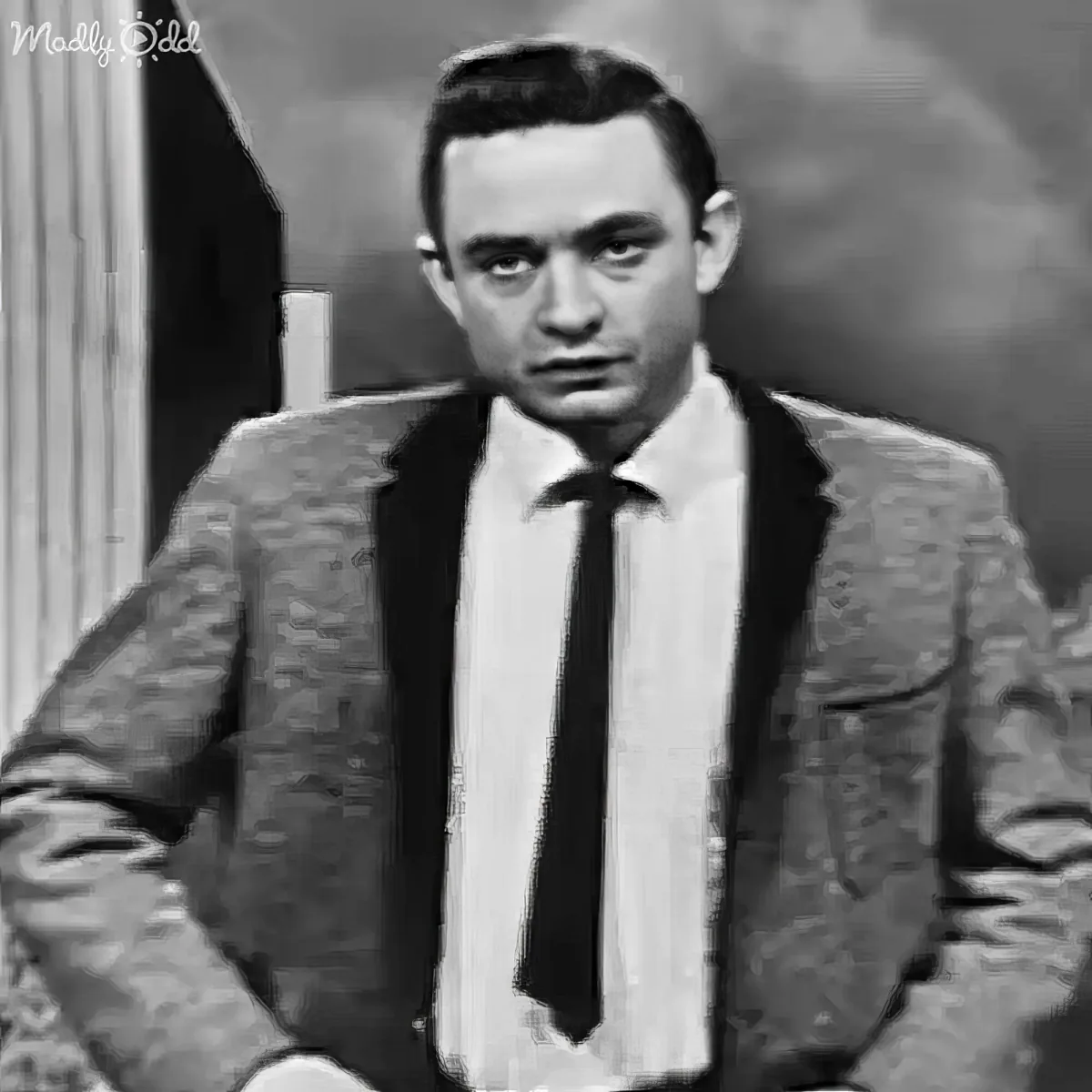 A man in a suit and tie sits with a serious expression, possibly from a classic film or TV show.