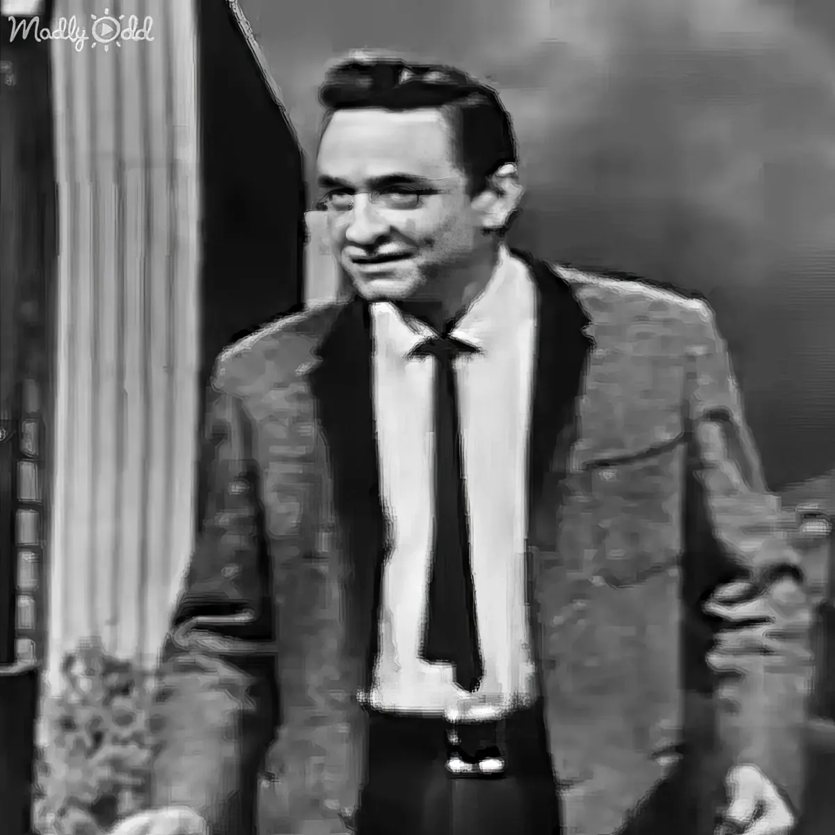 A man in a suit and tie smiles, standing in front of a curtain backdrop.