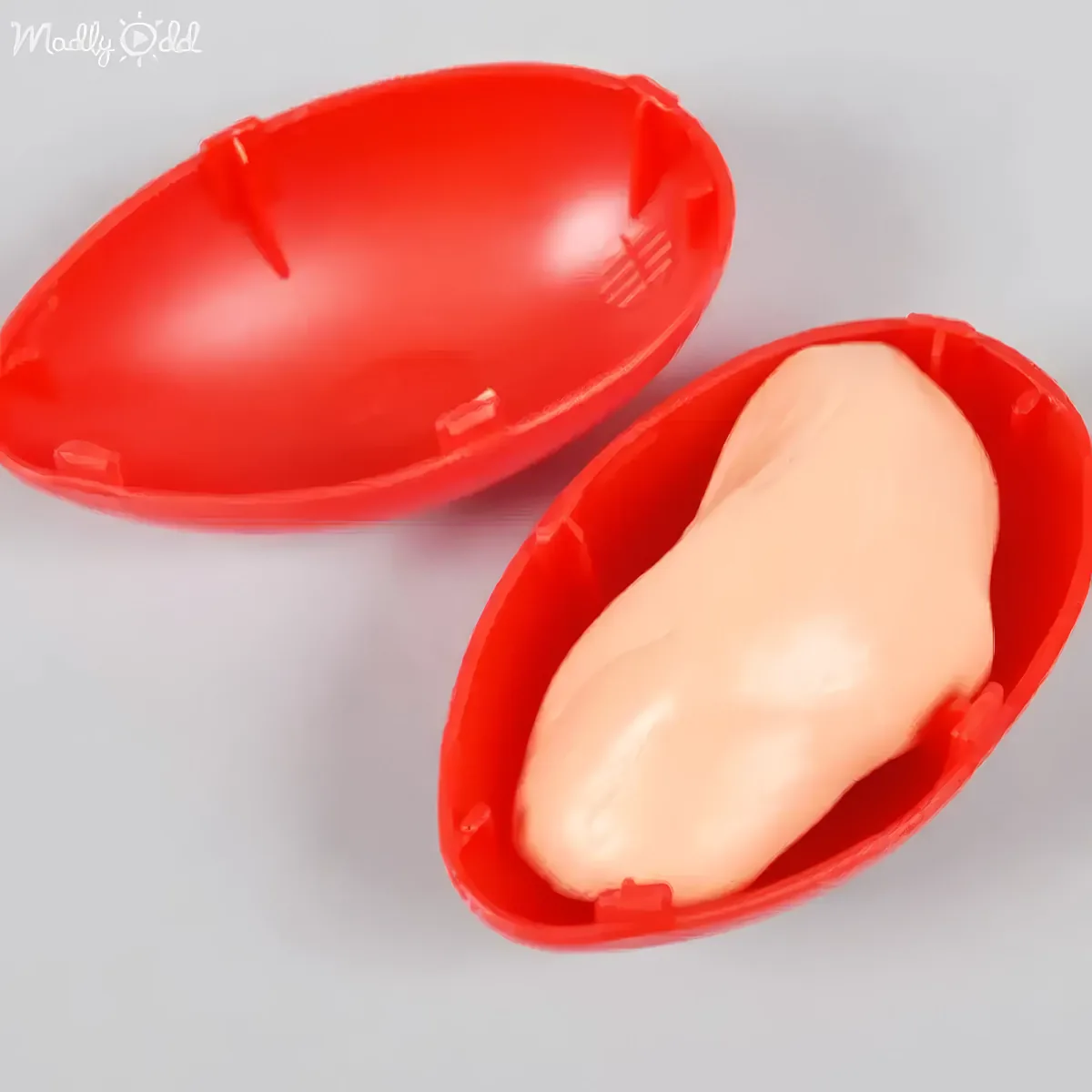 Two red plastic egg-shaped containers, one with a pale pink object inside, on a white surface.