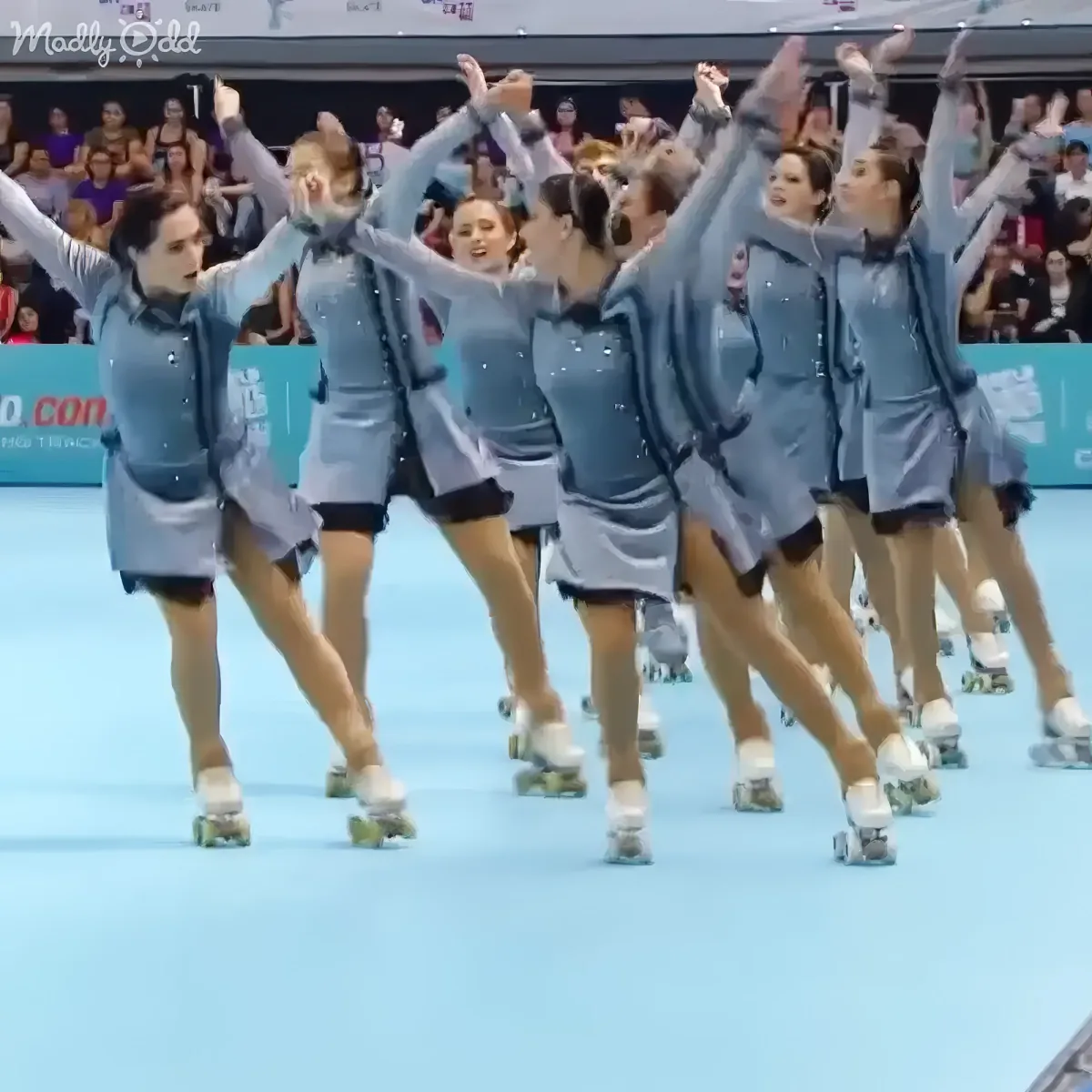 A synchronized roller skating team in matching outfits performs a routine on a light blue rink.