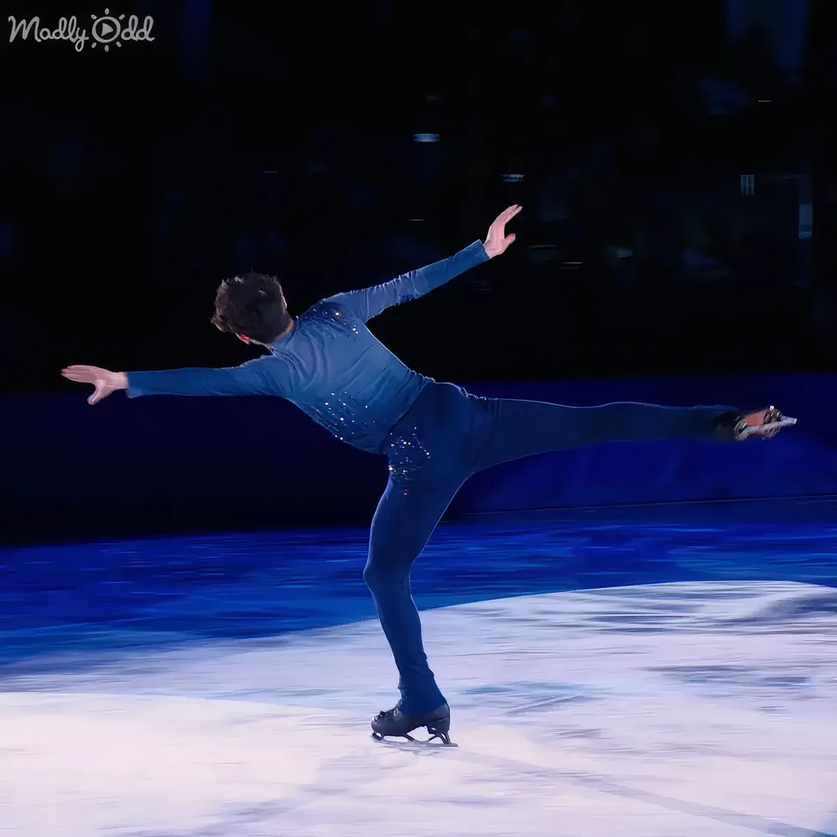 A figure skater in a blue outfit performs a graceful pose on the ice.