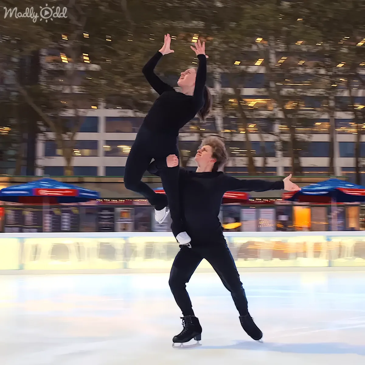 A skater lifts another in a synchronized ice skating performance on an outdoor rink.