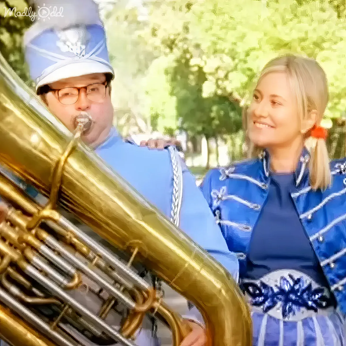 A man in a marching band uniform plays a large brass instrument while a woman in a blue jacket smiles beside him.