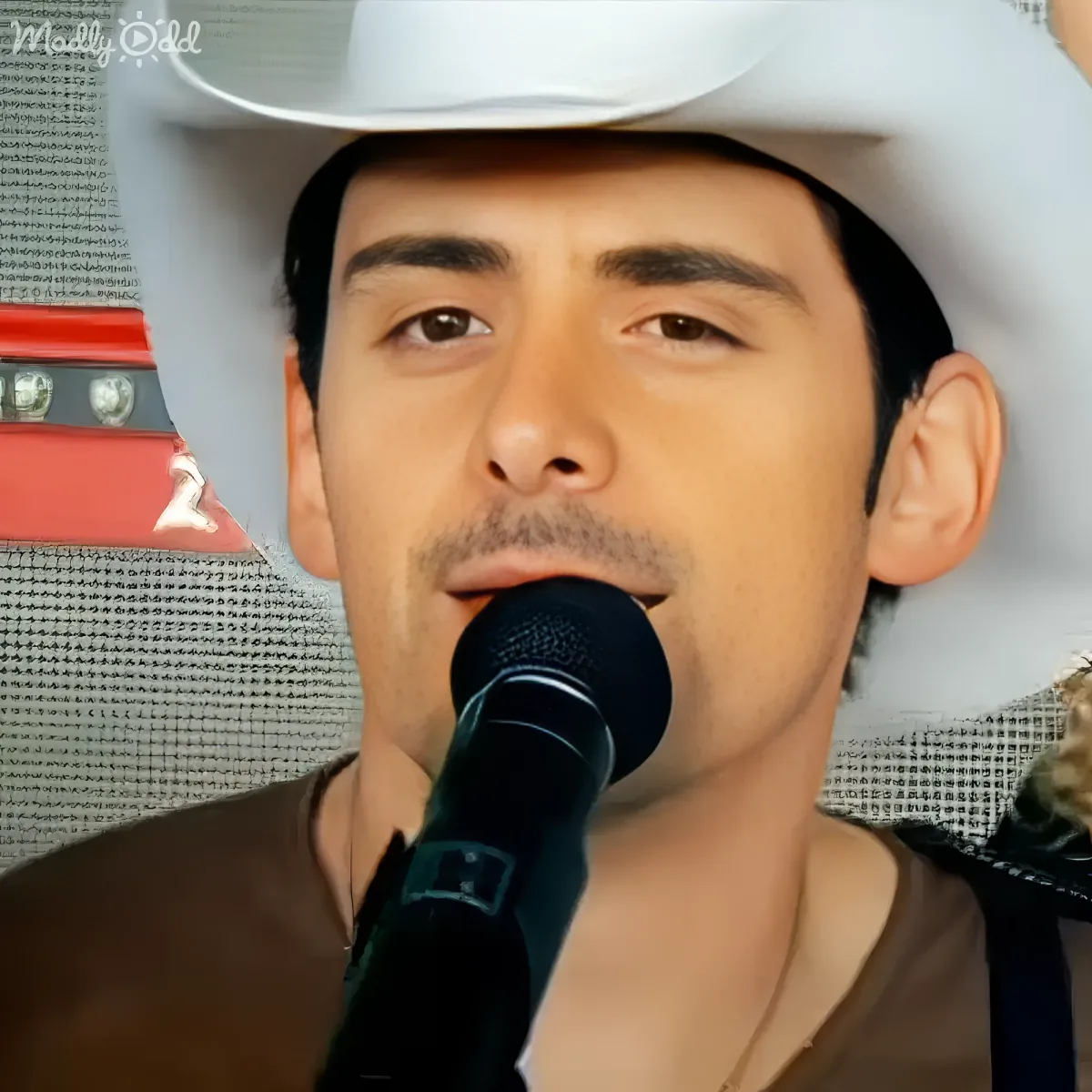 A man wearing a white hat sings into a microphone, with a red and white background.