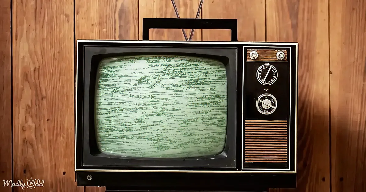 An old-fashioned television with static on the screen sits against a wooden wall.