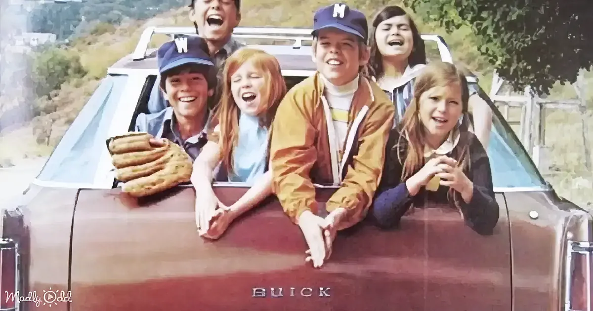 Six children in a vintage Buick, leaning out of the car window, laughing and enjoying the ride.