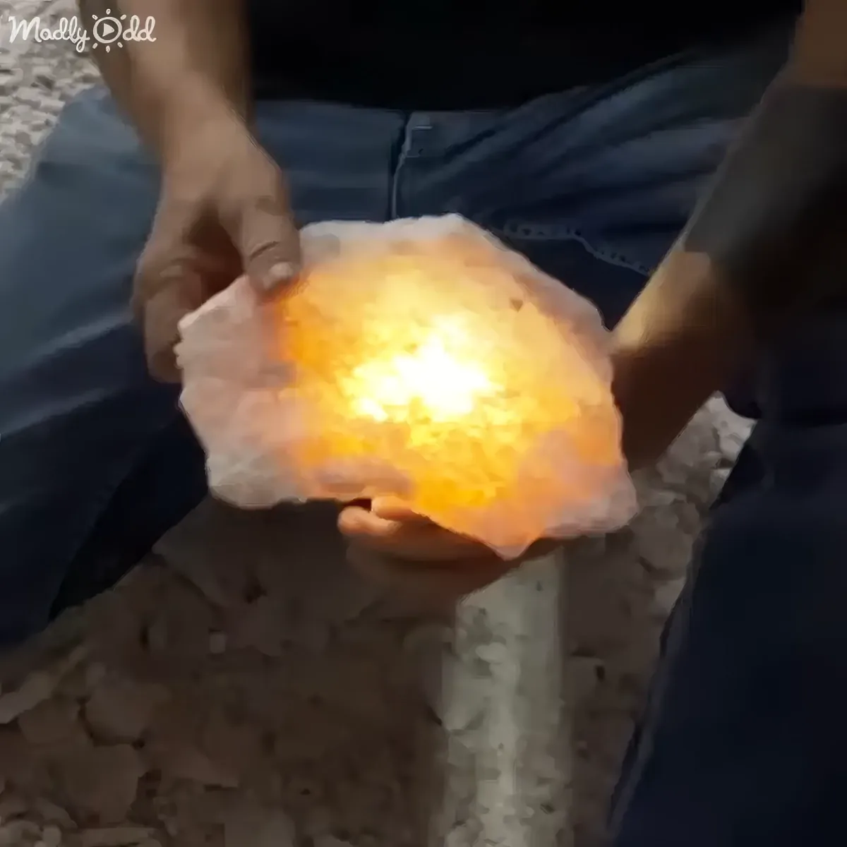 A person holds a glowing, orange, crystalline rock, emitting a bright light.