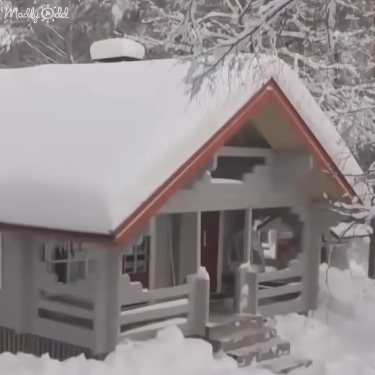 A snow-covered house with a red roof and a wooden porch surrounded by snow.
