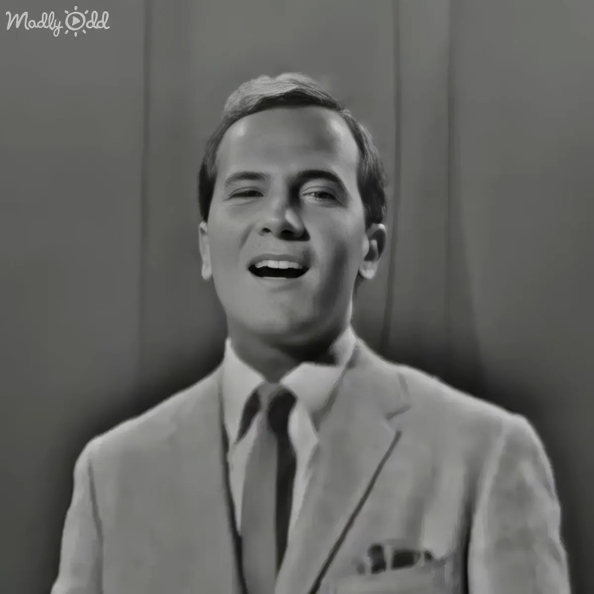 A man in a suit and tie smiles widely, wearing a white shirt and dark tie.