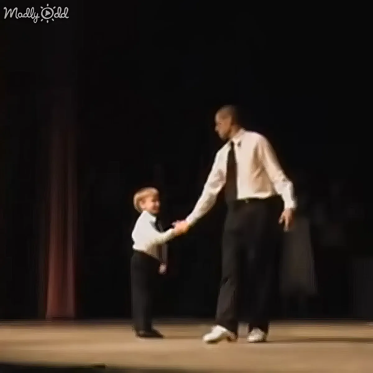 A man and a young boy are dancing together on a stage, holding hands.