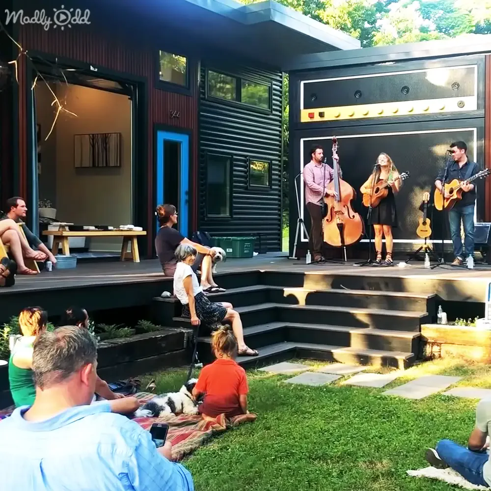 A band performs on a stage while a crowd enjoys the music in a backyard setting.