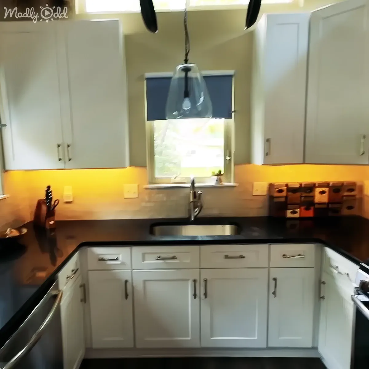A modern kitchen with white cabinets, black countertops, and a hanging light fixture above the sink.