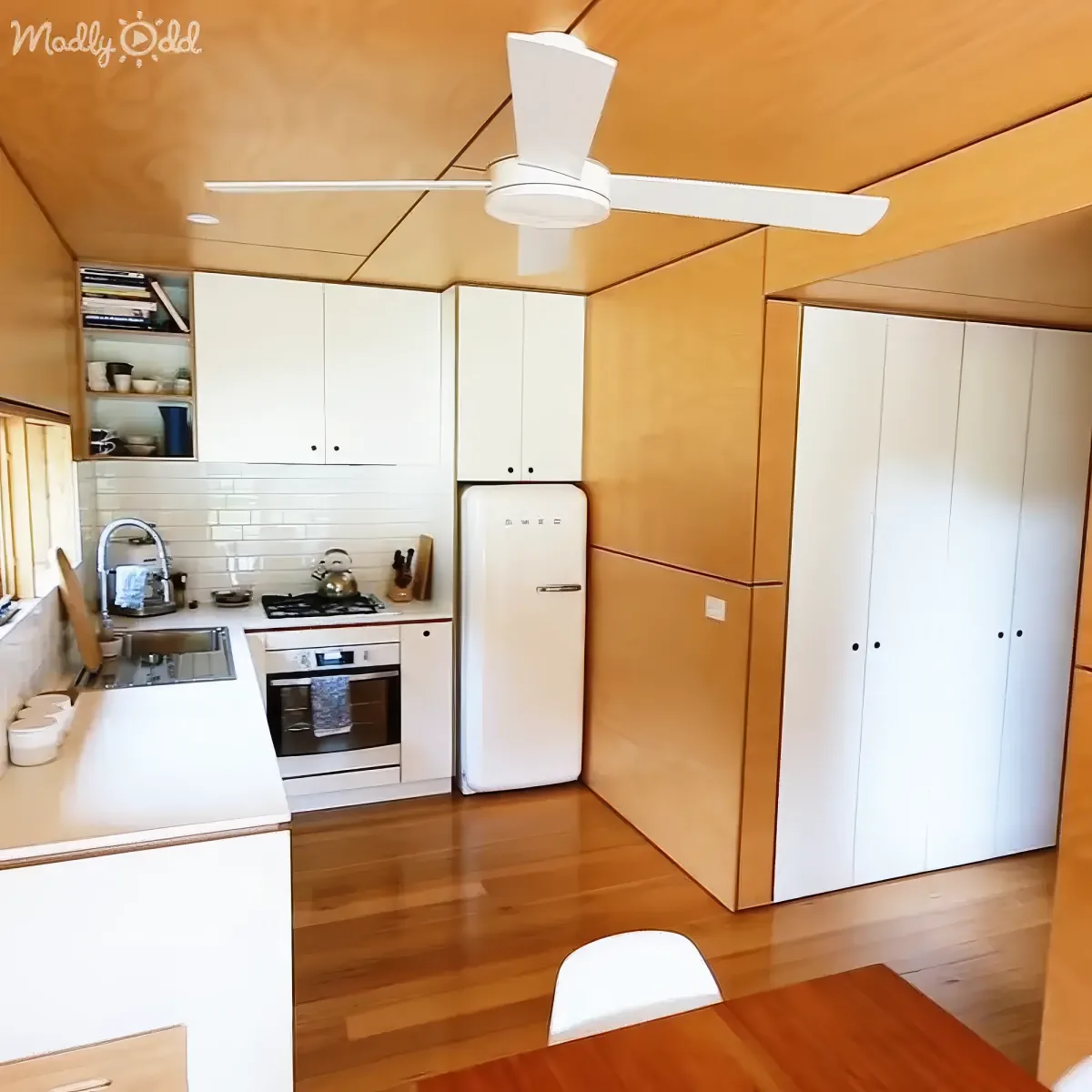 A cozy kitchen with white cabinets, a retro Smeg refrigerator, and a wooden ceiling fan.