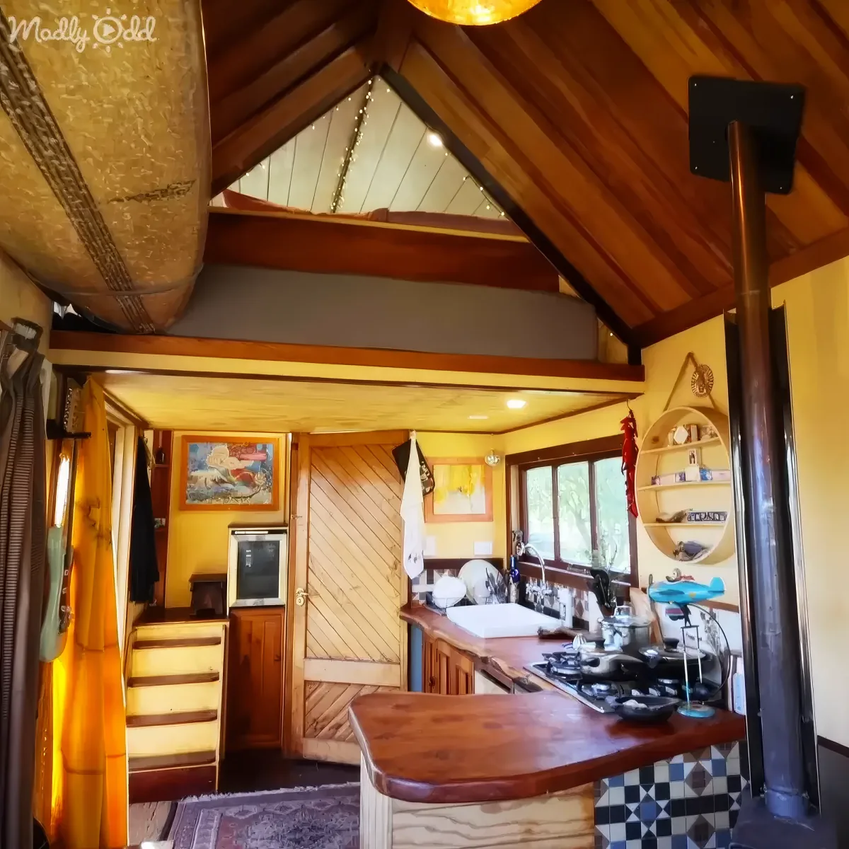 A cozy, rustic kitchen with wooden beams, a surfboard on the wall, and a small stove with pots and pans.