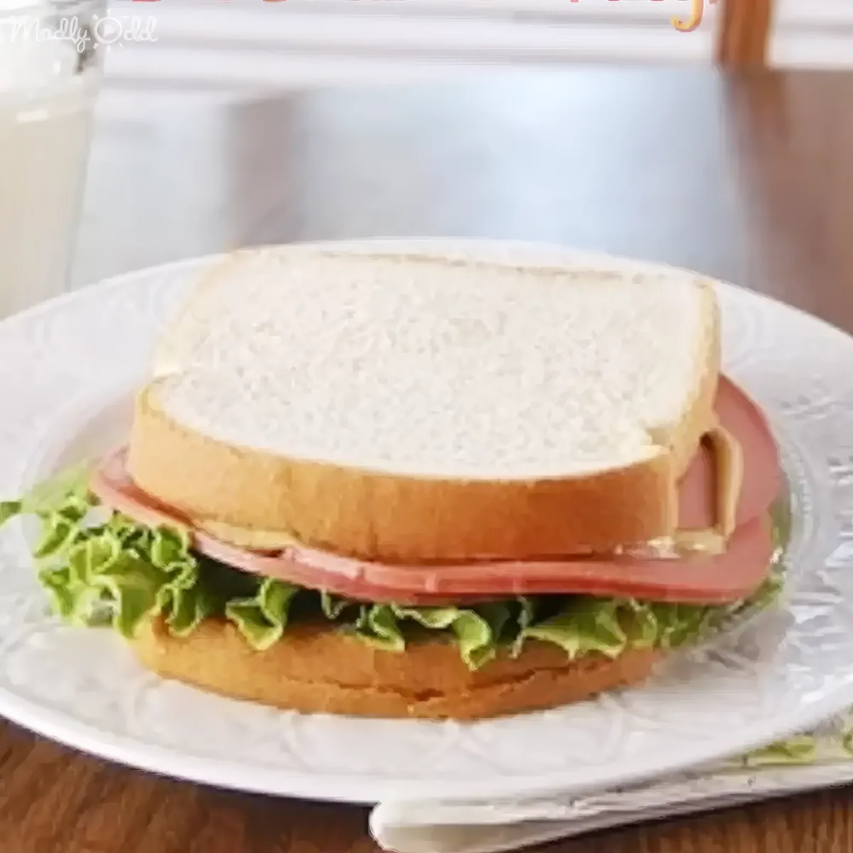 A sandwich with lettuce and ham on white bread sits on a decorative plate.