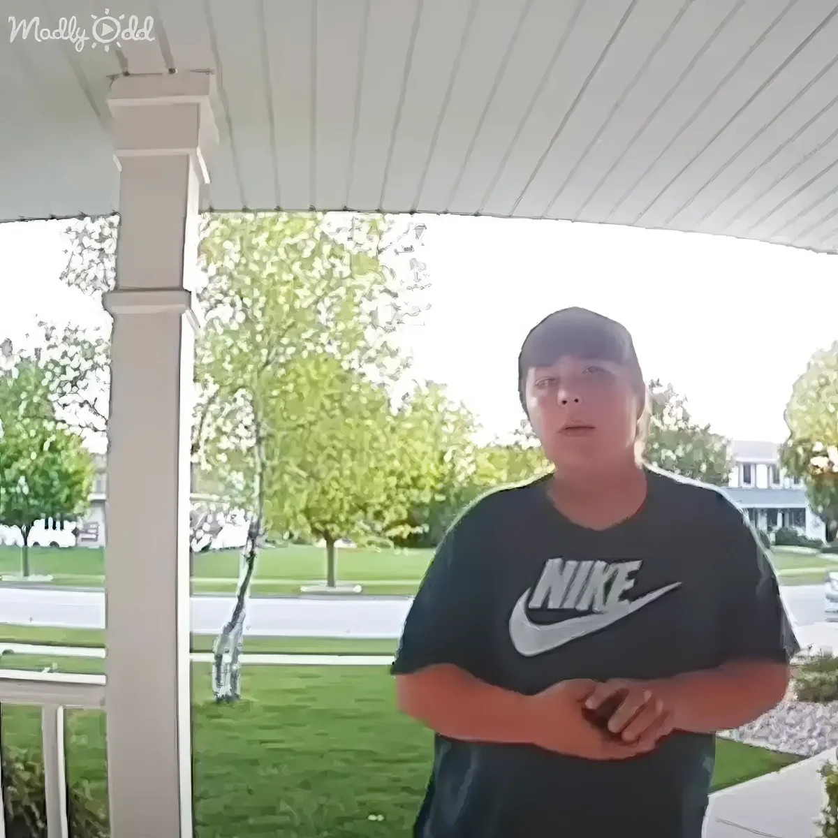 A person in a Nike shirt stands on a porch, with trees and a house in the background.