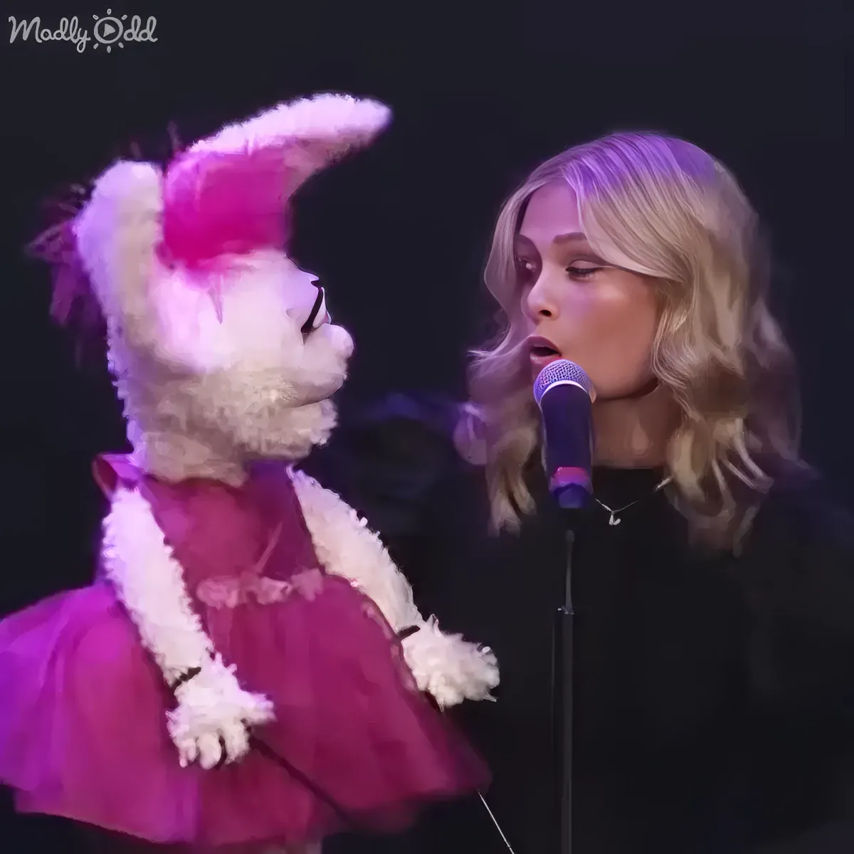 A person in a costume resembling a llama stands next to another person holding a microphone.