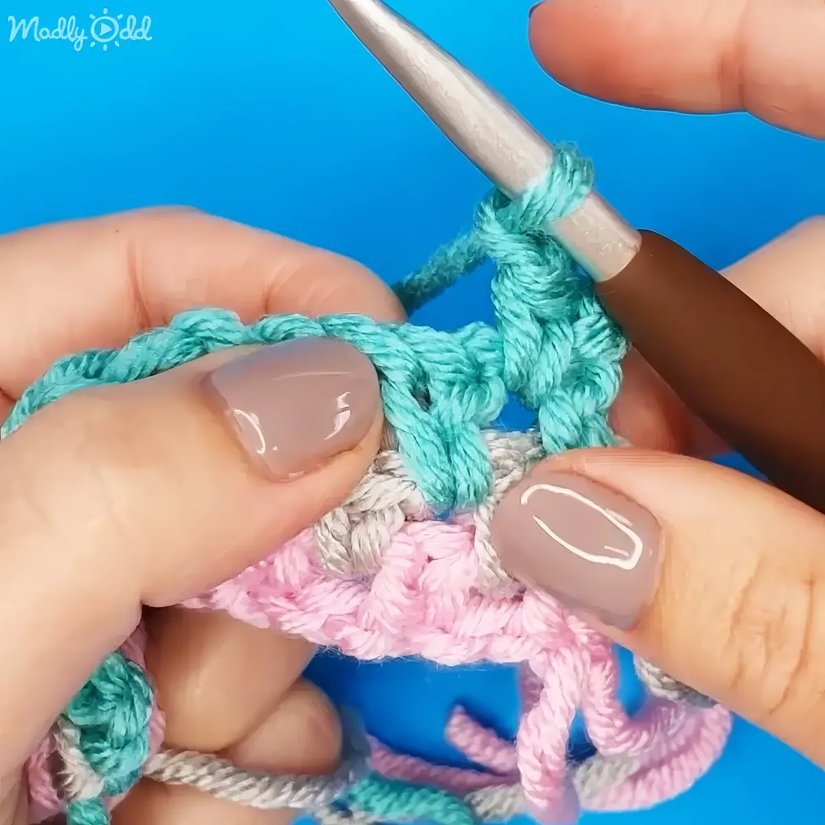 A hand holds a crochet hook and yarn, creating a colorful fabric with intricate loops.