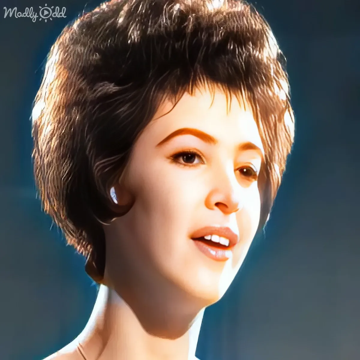 A person with short, dark hair and a white top is shown in a close-up, with a light source highlighting their face.