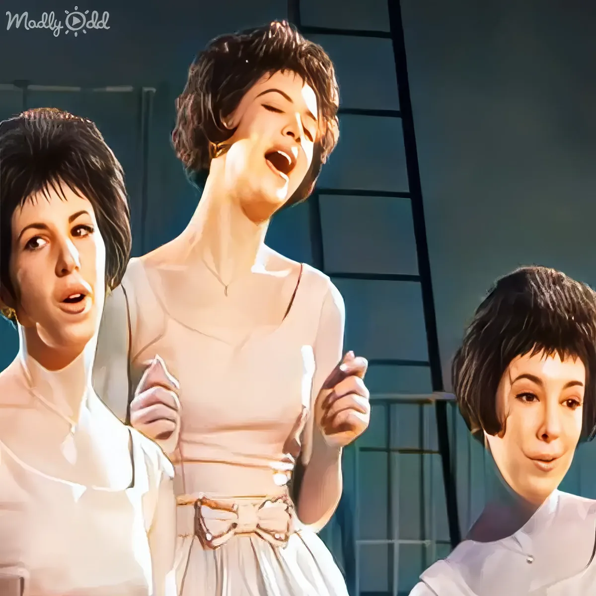 A woman in a light pink dress sings passionately, flanked by two others in white, against a backdrop of a window.