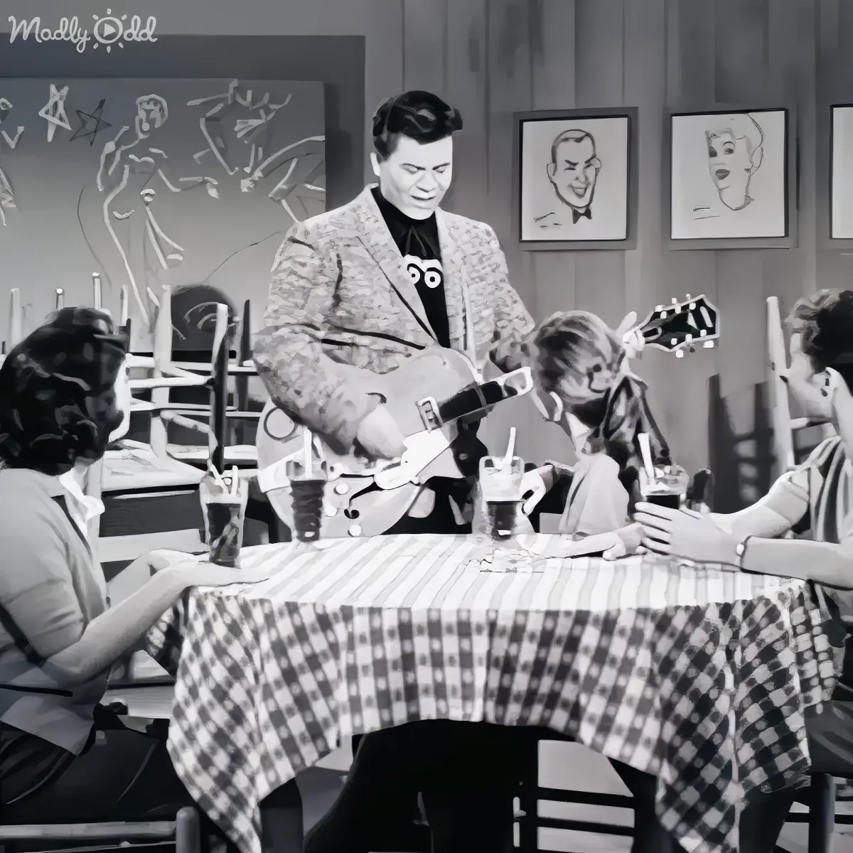 A man plays guitar at a diner table with three seated customers, all wearing masks.