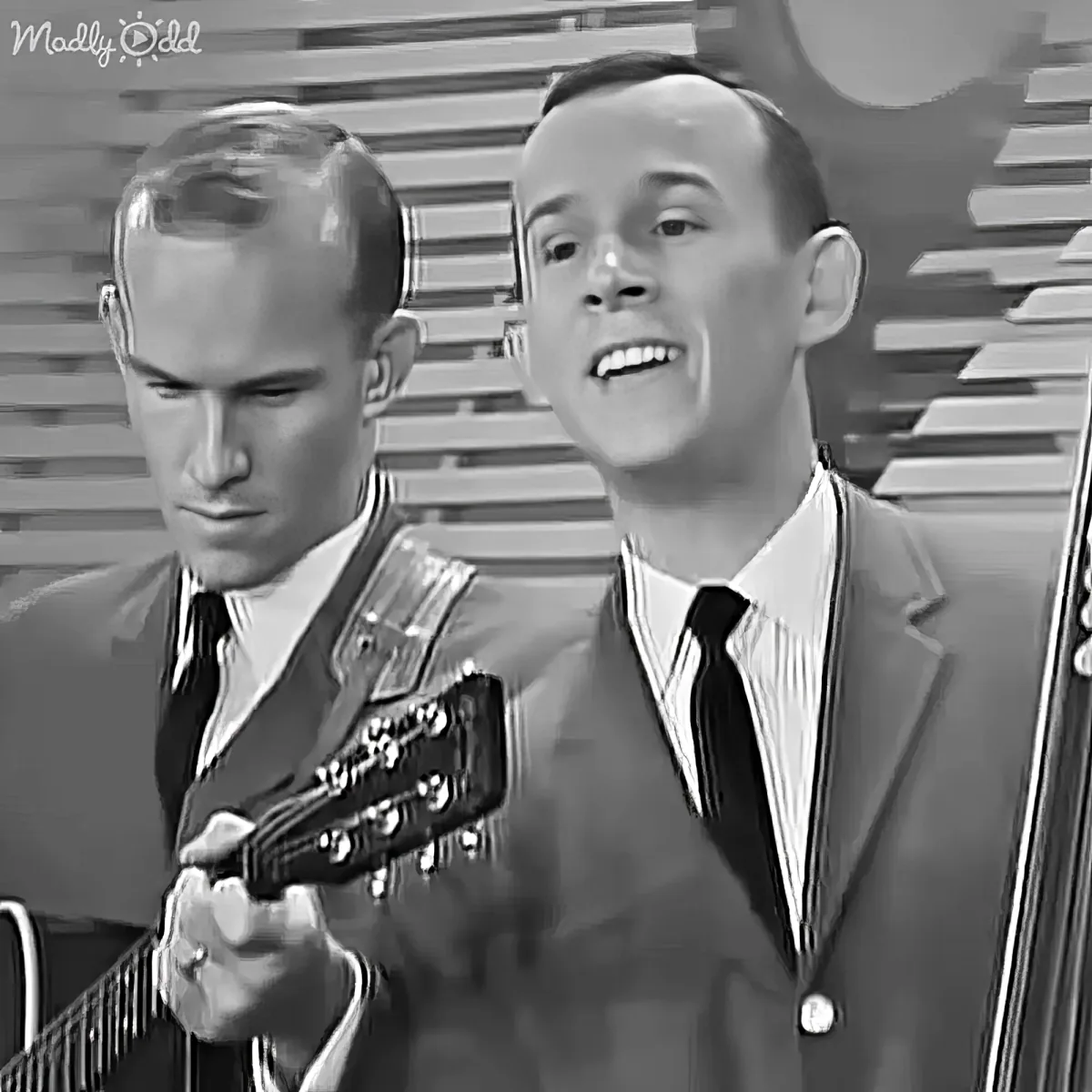 Two men in suits, one playing guitar, both smiling, vintage black-and-white image.