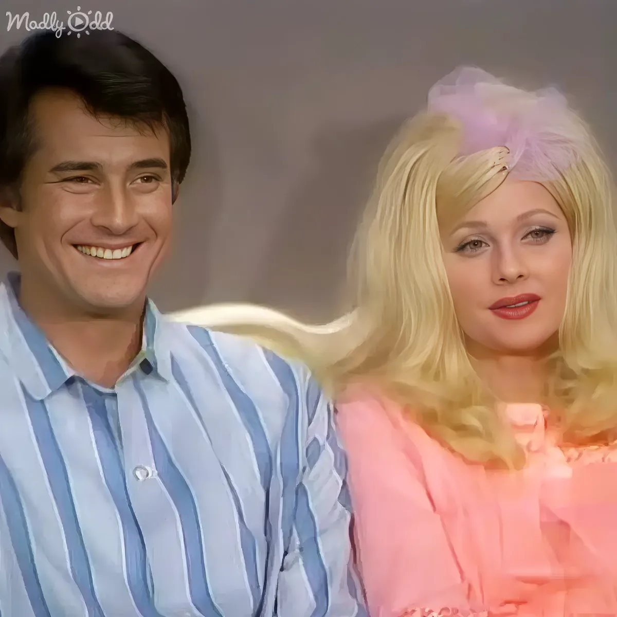 A man in a striped shirt smiles next to a woman in a pink dress with a flower in her hair.