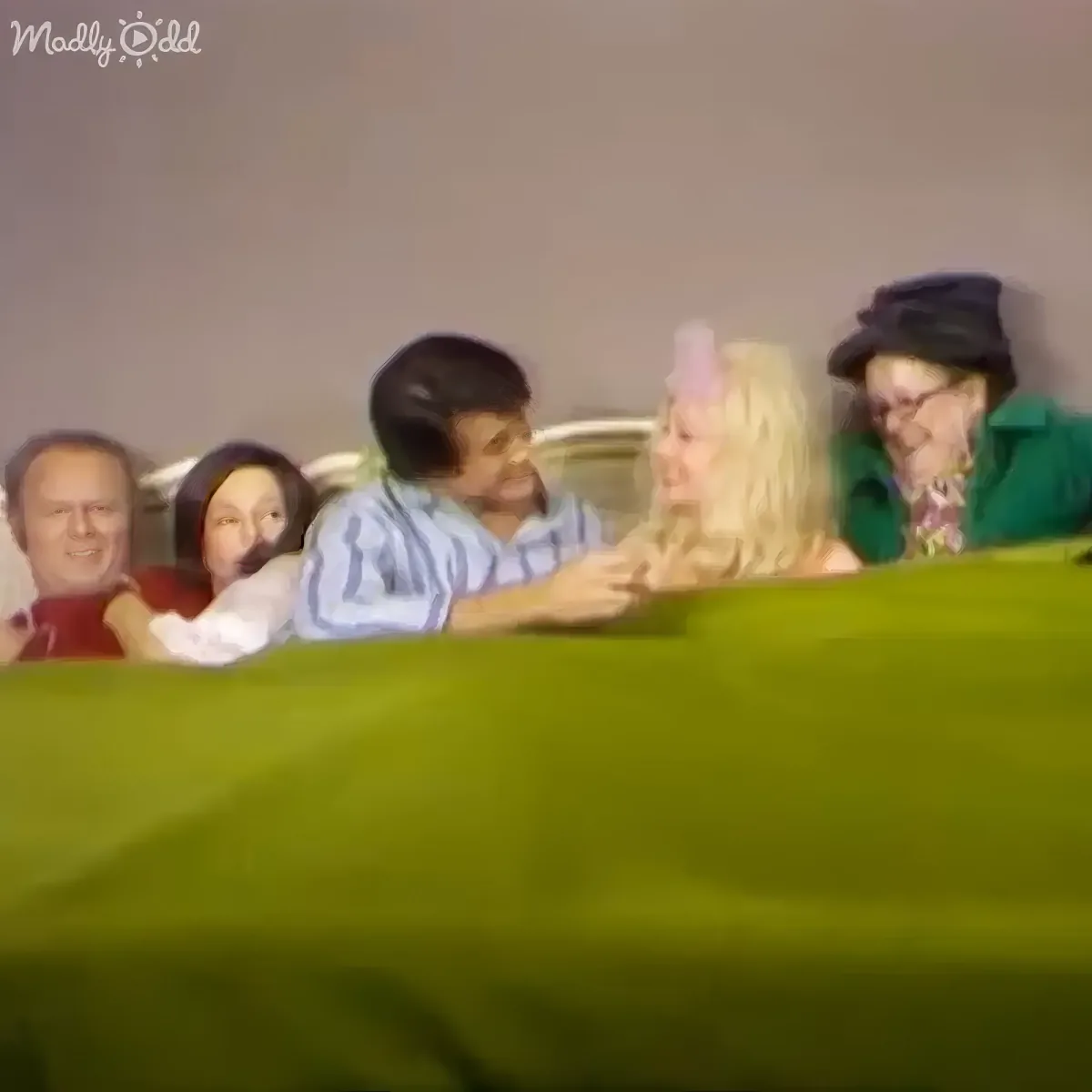 A person in a striped shirt is interacting with a blonde-haired individual, while others watch in the background.