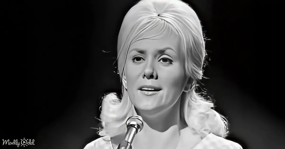 A woman with blonde hair styled in a bun, wearing a white outfit, singing into a microphone.