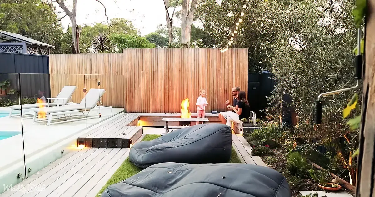 A family enjoys a cozy backyard with a fire pit, bean bags, and lounge chairs surrounded by greenery.