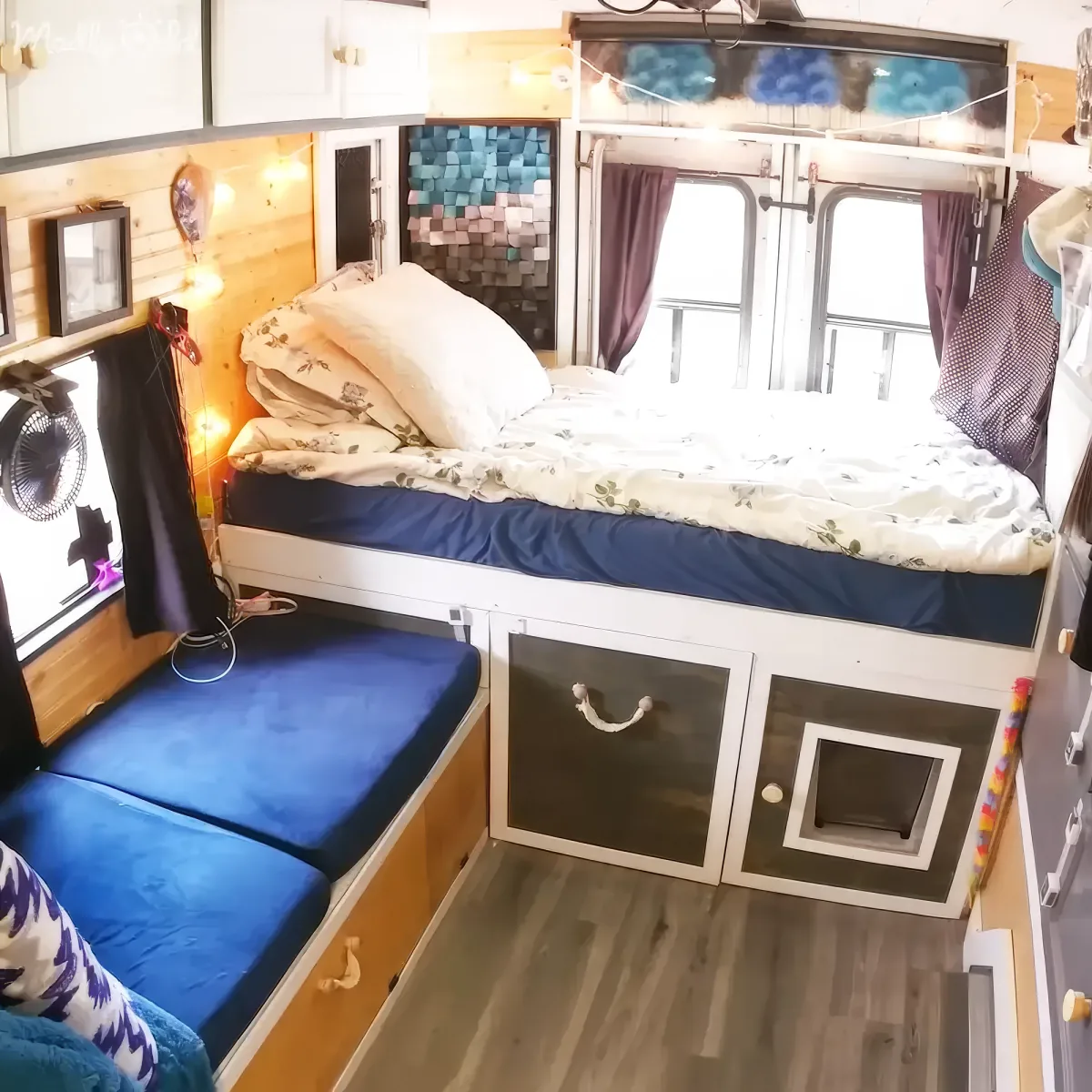 A cozy, compact bedroom with a bed, storage drawers, and string lights, featuring a blue and white color scheme.