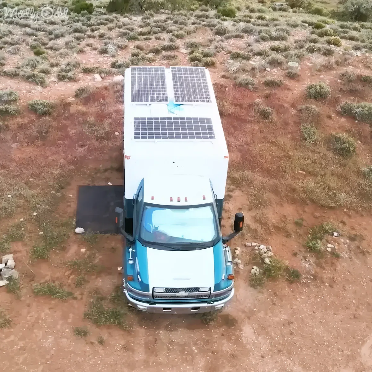 A white and blue van with solar panels on the roof is parked in a dry, grassy field.