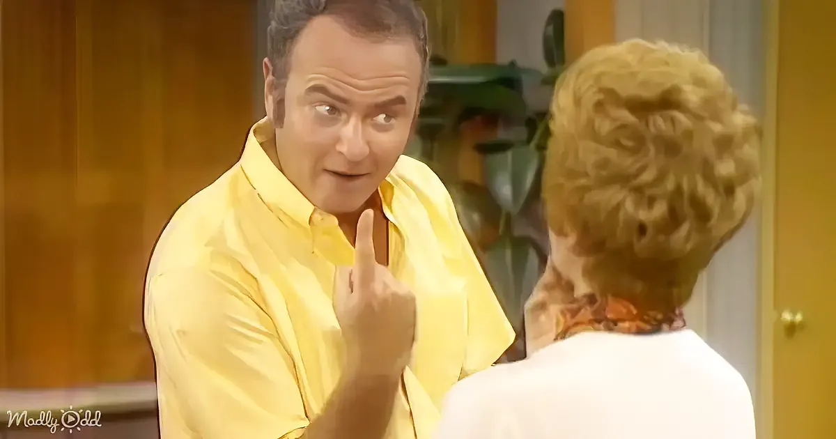 A man in a yellow shirt points upwards while talking to a woman with curly blonde hair.