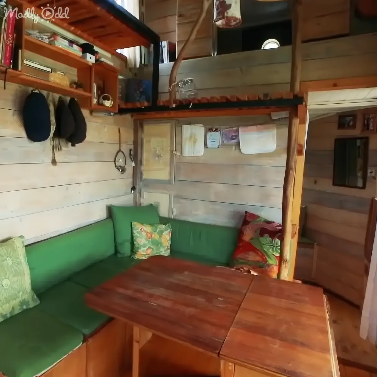 A cozy, rustic interior with a green couch, wooden table, and shelves holding books and hats.