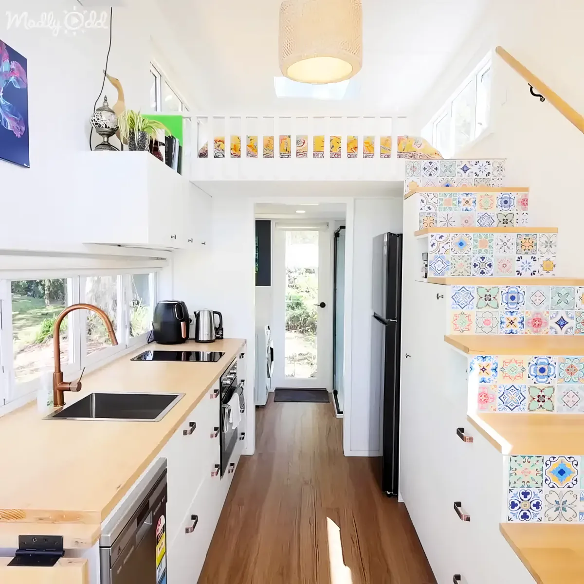A cozy kitchen with wooden countertops, a copper faucet, and colorful tiled stairs leading to a loft.