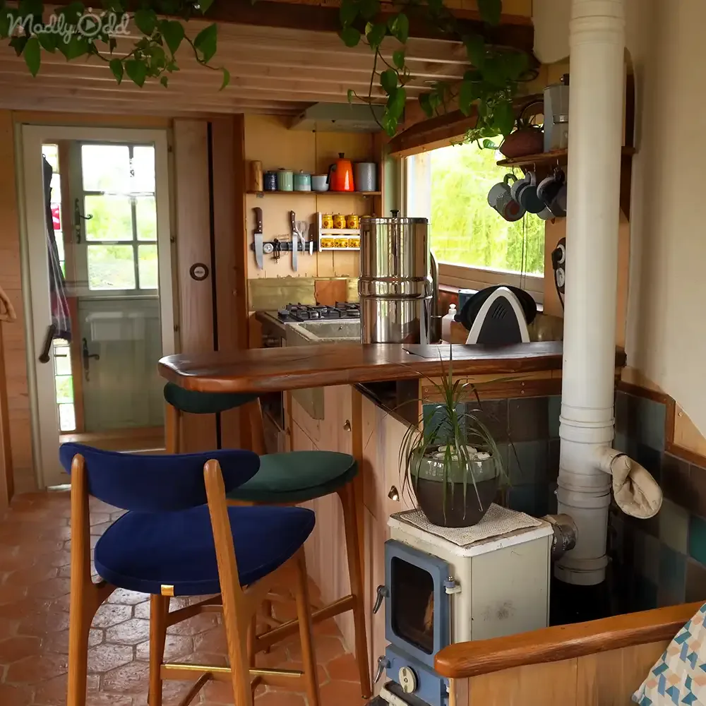 A cozy kitchen with a wooden bar, stools, a wood-burning stove, and hanging plants.
